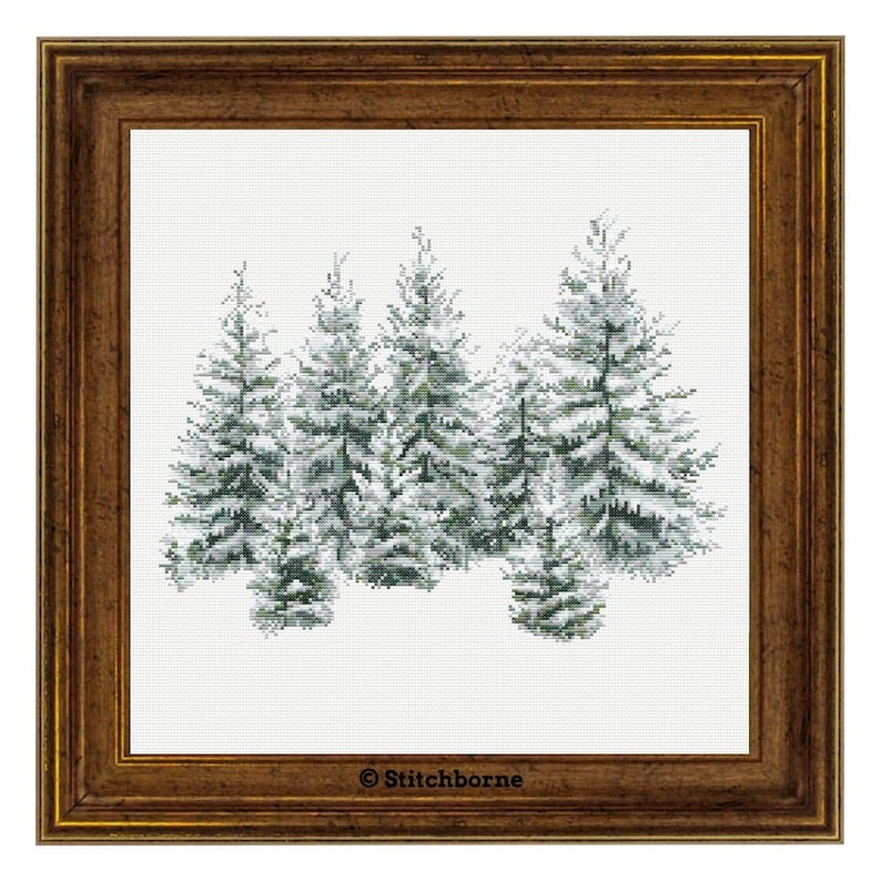 May include: A framed cross-stitch depicting a cluster of snow-covered evergreen trees. The trees are detailed with shades of green and white, set against a white background. The frame is a warm, dark brown color, adding a rustic touch.