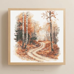 May include: A framed cross-stitch landscape showing an autumnal forest scene. It features a winding dirt track leading into the distance, surrounded by trees with orange and brown leaves. The frame is made of light-coloured wood.