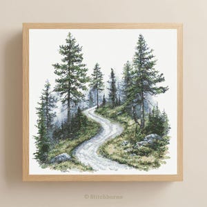 May include: Cross-stitch art of a winding forest road, framed in a light wood. The scene features tall green trees, a misty atmosphere, and a textured path. The artwork is signed "Stitchborne" in the bottom corner.