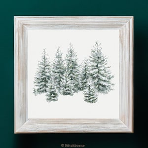 May include: A framed cross-stitch artwork featuring a winter forest scene. The image shows several snow-covered evergreen trees in shades of green and white. The artwork is set in a rustic, light-colored wooden frame, perfect for home decor.