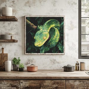 May include: A framed artwork depicting a green snake coiled on a branch, surrounded by green leaves. The snake has yellow markings and is the focal point. The artwork is displayed in a kitchen with a rustic aesthetic.