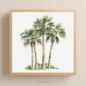 May include: A framed cross-stitch artwork featuring a cluster of palm trees. The trees have green fronds and textured brown trunks, set against a white background. The artwork is enclosed in a light-colored wooden frame, creating a tropical theme.