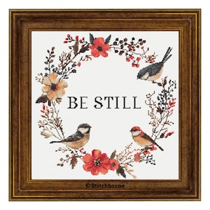 Könnte beinhalten: Kreuzstichmuster mit einem Blumenkranz mit roten und weißen Blumen, zwei Vögeln und dem Text "BE STILL".