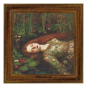 Op de afbeelding: Kruissteekkunstwerk van een vrouw in een groene jurk die in het water drijft, omringd door waterlelies en riet. Het kunstwerk is ingelijst in een goudkleurige houten lijst. De vrouw heeft lang rood haar en ligt met gesloten ogen. Het kunstwerk is gesigneerd "© Stitchborne".