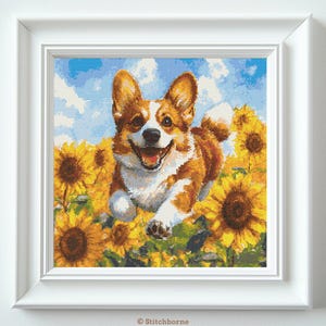 May include: A framed cross-stitch artwork depicts a happy corgi dog running through a field of sunflowers. The dog has brown and white fur, a smiling expression, and is set against a blue sky with white clouds. The sunflowers are yellow and brown.