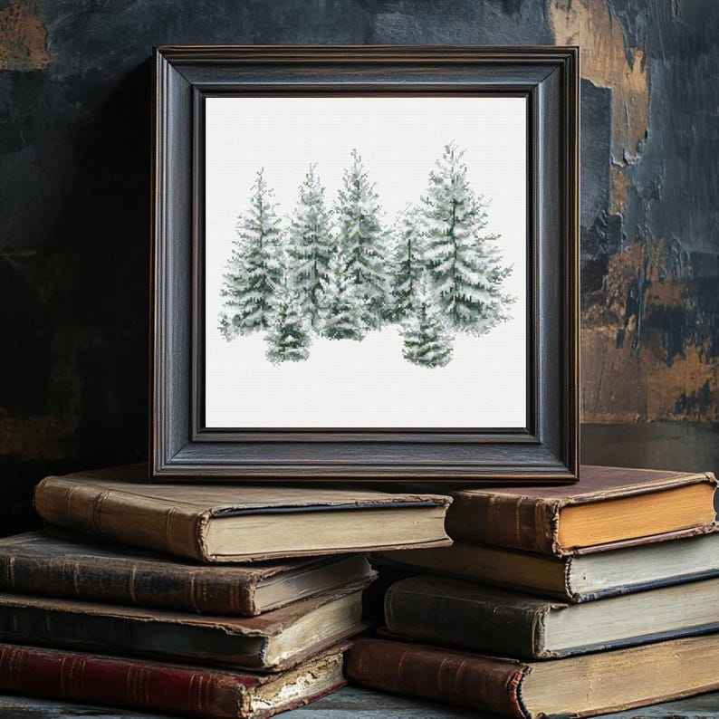 May include: A framed print featuring a watercolor painting of several snow-covered evergreen trees. The artwork is set against a white background and framed in a dark, rustic wooden frame. The frame rests on a stack of antique books.