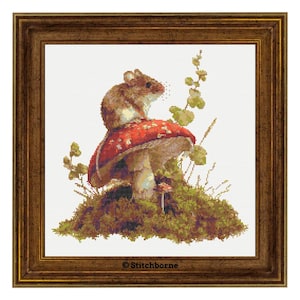 May include: Cross-stitch art of a mouse sitting on a red and white mushroom, surrounded by greenery and moss. The artwork is framed in a brown wooden frame. The image has a whimsical, nature-inspired theme.