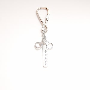 May include: Silver keychain with a silver charm that says "BRAVE" and two silver handcuffs.
