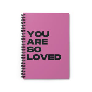 以下が含まれることがあります： 鮮やかなピンク色の表紙に「YOU ARE SO LOVED」の文字が黒い太字で印刷された、スパイラル綴じのノート。ノートは黒い金属製のスパイラルバインディングです。