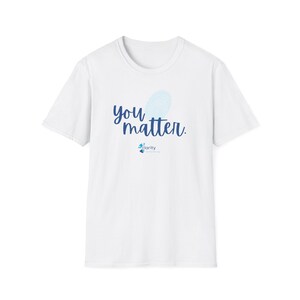 以下が含まれることがあります： 「you matter」という青い筆記体の文字と青い指紋のデザインが施された白いTシャツ。テキストの下には、小さな青いグラフィックとともに、青い筆記体で「clarity」という文字が書かれています。