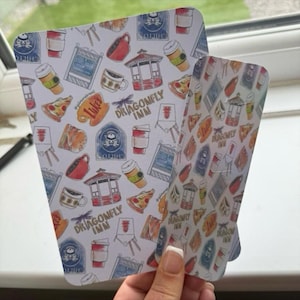 May include: Two decorative paper cutouts with a repeating pattern of coffee cups, pizza slices, and the text "Dragonfly Inn". The cutouts are white with a variety of colorful illustrations.