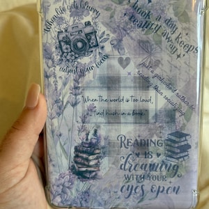 Könnte beinhalten: Eine transparente Schutzhülle für einen E-Reader mit Lavendel-Blumenmuster und Text. Das Design umfasst eine Vintage-Kamera-Illustration und Sätze wie "Wenn das Leben verschwimmt, passe deinen Fokus an" und "Lesen ist Träumen mit offenen Augen".