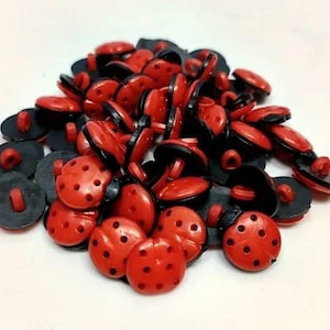 May include: A pile of red and black ladybug buttons with black centres and white dots. The buttons are approximately 2.5 cm in diameter.