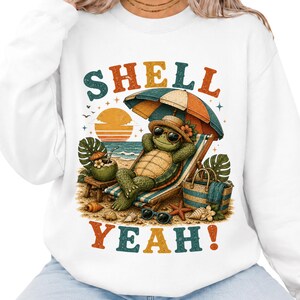May include: A white sweatshirt featuring a graphic of a turtle wearing a straw hat and sunglasses, lounging on a beach chair under an umbrella. The text reads SHELL YEAH! with a sunset, palm leaves, a coconut drink, and seashells on the sand.