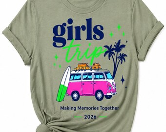May include: Olive green t-shirt featuring a pink and white van with luggage, a surfboard, and palm trees. The shirt has the words "Girls Trip" in blue and green, with "Making Memories Together 2026" below the van.