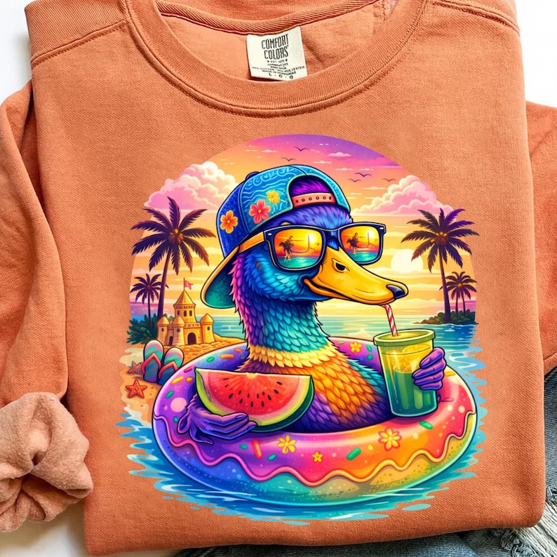 以下が含まれることがあります： オレンジ色のComfort Colorsスウェットシャツ。サングラス、帽子、ドーナツ型の浮き輪を身に着けた、カラフルな漫画のアヒルが描かれています。アヒルはスイカのスライスと飲み物を持っており、背景にはビーチのシーンがあります。