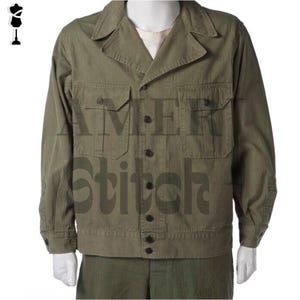 Può includere: Una giacca utility verde con chiusura a bottoni e due grandi tasche. La giacca ha un motivo a spina di pesce ed è realizzata in un tessuto resistente.