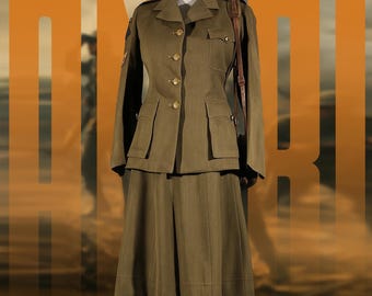 Op de afbeelding: Olijfgroen militair uniform bestaande uit een jasje en rok. Het jasje heeft vier zakken, gouden knopen en schouderstukken. Een bruine leren riem is over de schouder van de mannequin gedrapeerd. De rok is knielang. De achtergrond heeft oranje tekst.