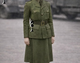 Op de afbeelding: Een olijfgroene militaire uniform bestaande uit een jas, rok en riem. De jas heeft vier zakken en goudkleurige knopen. De rok is knielang. De riem heeft een goudkleurige gesp. Het uniform wordt gedragen met een bijpassende hoed en stropdas.