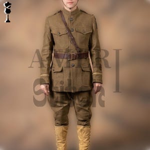 Puede incluir: Un uniforme militar verde oliva, que incluye una chaqueta de cuello alto con cuatro bolsillos, pantalones a juego y un cinturón y bandolera de cuero marrón. El conjunto incluye un casco y botas altas de color beige. El uniforme recuerda a la indumentaria militar histórica.