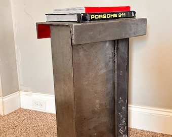Op de afbeelding: Een metalen bijzettafel met een rood blad en een boek met de titel "PORSCHE 911" erop.