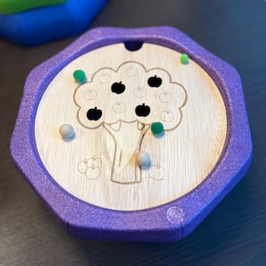 Può includere: Puzzle in legno a forma di albero di mele con cornice esagonale viola. L'albero ha ritagli di mele nere e mele a pompon verdi. Due palline di legno e pompon verdi sparsi. Per bambini.