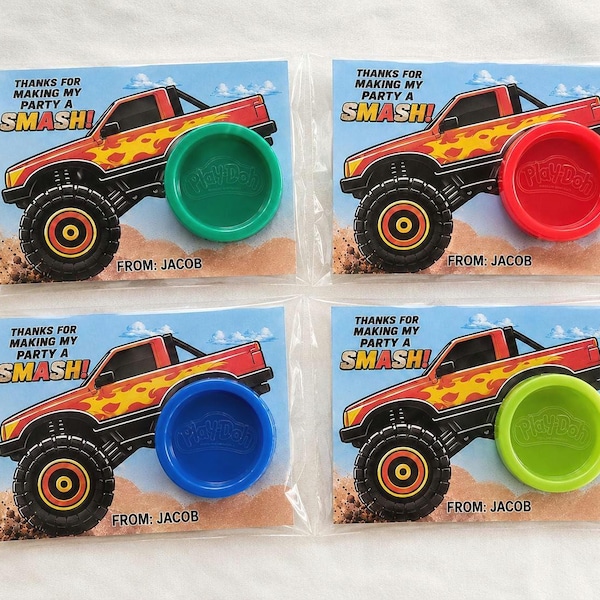 Pode incluir: Quatro cartões de lembrancinha em embalagens plásticas transparentes, cada um com um monster truck vermelho com chamas amarelas, o texto THANKS FOR MAKING MY PARTY A SMASH! e FROM: JACOB. Cada cartão inclui uma tampa Play-Doh redonda.