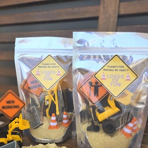 May include: Clear cellophane bags filled with sand, toy construction vehicles, and orange and white traffic cones. Each bag has a yellow and white label that reads "THANKS FOR MAKING MY PARTY" and "LOADS OF FUN!"