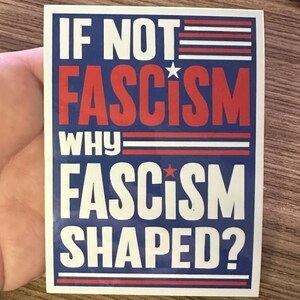 May include: A white sticker with blue and red stripes and stars. The sticker has the text "IF NOT FASCISM WHY FASCISM SHAPED?" in white letters.