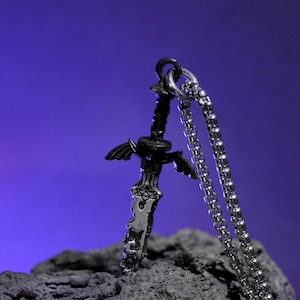 May include: A silver-colored pendant necklace featuring a detailed sword design with a pentagram on the blade and wing-like accents. The sword hangs from a chain necklace, set against a dark purple background.