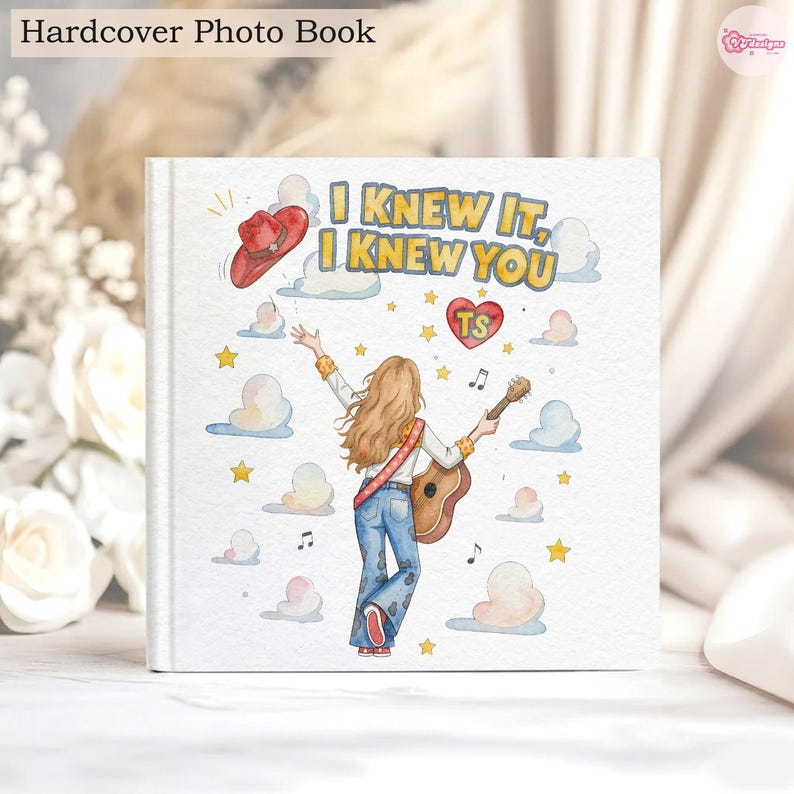 May include: A square hardcover photo book featuring a watercolour illustration of a person with long hair playing an acoustic guitar. The text reads I KNEW IT, I KNEW YOU, accompanied by a red cowboy hat, a heart with TS, stars, and clouds.