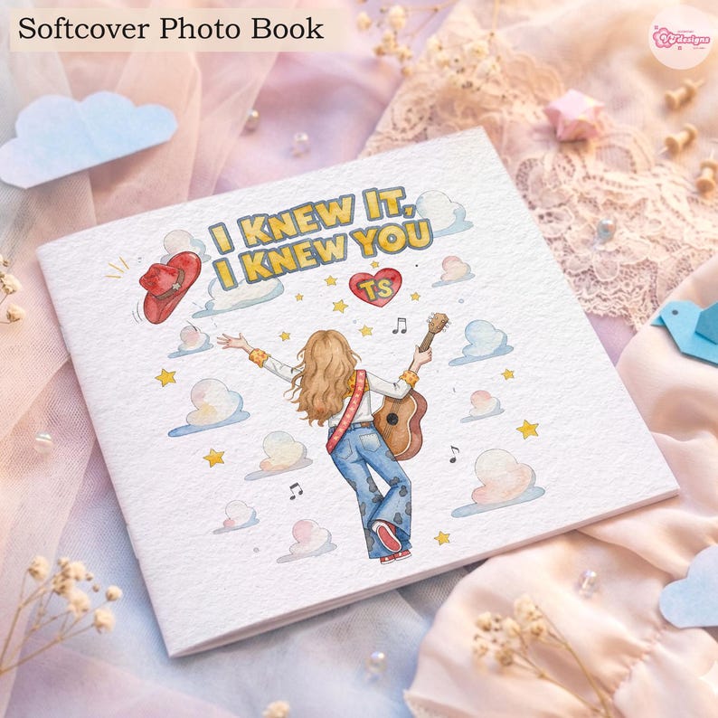 May include: A square softcover photo book featuring a white cover with a central illustration of a person with long hair playing an acoustic guitar. The text reads I KNEW IT, I KNEW YOU with a red cowboy hat, a heart labelled TS, stars, and clouds.