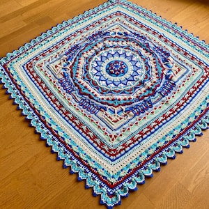 May include: A crocheted square blanket with a colorful mandala design in the center. The blanket is made with a variety of blues, reds, and greens.