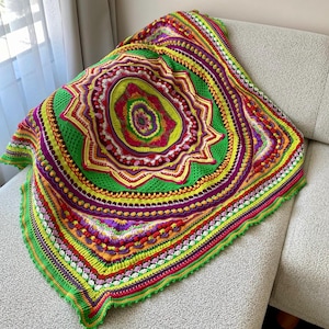 May include: A vibrant, handmade crochet blanket with a circular, mandala-like design. The blanket features a bright color palette of green, purple, yellow, and red. The intricate pattern includes textured stitches and a scalloped edge, creating a cozy and decorative textile.