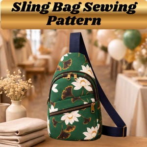 Op de afbeelding: Groen sling bag naaipatroon met een bloemenontwerp met witte bloemen en bruine bladeren. De tas heeft een marineblauwe band en gouden ritsen. De tekst "Sling Bag Sewing Pattern" wordt bovenaan weergegeven.