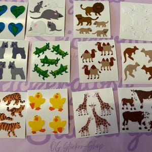 Puede incluir: Una colección de hojas de pegatinas con varios diseños de animales y naturaleza. Las pegatinas incluyen leones, tigres, jirafas, patos y osos polares. Las pegatinas están sobre un fondo morado claro.