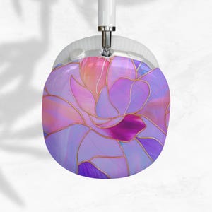 Könnte beinhalten: Weiße und silberne Kopfhörer mit floralem Design. Der Ohrmuschel hat ein lila, rosa und goldfarbenes Muster im Glasmalerei-Stil. Die Kopfhörer haben ein weißes Kopfband und silberne Akzente.