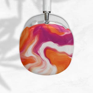 May include: White over-ear headphones with a colorful design. The ear cup features a swirling pattern of orange, pink, and white. The headband and other components are white. The headphones are suspended against a white background.