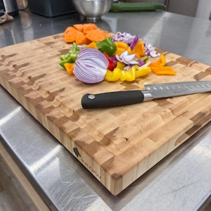 May include: A light-coloured wooden butcher block cutting board with a black handle knife and chopped vegetables. The board has a textured surface and the words "BLACK WOLF" are printed on the side.