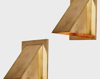 May include: A pair of wall-mounted sconces featuring a rectangular backplate and a triangular, wedge-shaped metal shade. The brass-toned metal has a warm, muted finish, and the design directs light downward from the open bottom of the fixture.