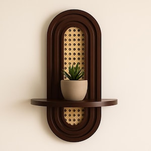 May include: A dark brown wooden wall shelf with an arched frame and a central panel of light tan woven cane webbing. A small, matte beige ceramic pot containing a green artificial succulent plant sits on the horizontal shelf surface.