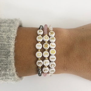 May include: Three white beaded bracelets with gold lettering spelling out the words "Rejoice", "Do Well", and "Abide".