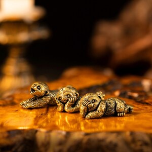 May include: Three small, antique-style brass sloth figurines in different poses. One sloth is lying down with its mouth open, the second is resting its head on its hands, and the third is covering its eyes with its paws. Each piece has a textured finish.