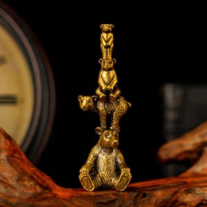Può includere: Una scultura in ottone dettagliata di quattro orsi impilati uno sull'altro. Gli orsi sono in posizione seduta e in piedi, con l'orso più piccolo in cima. La scultura ha un colore dorato ed è ambientata su uno sfondo scuro.