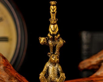 May include: A detailed brass sculpture of four bears stacked on top of each other. The bears are in a sitting and standing position, with the smallest bear at the top. The sculpture has a golden color and is set against a dark background.