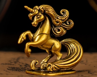 May include: A golden unicorn figurine in a rearing pose. The sculpture has a detailed mane and tail, and a prominent horn. The figurine is made of a shiny, metallic material and sits on a rectangular base. The background is dark, highlighting the gold color.