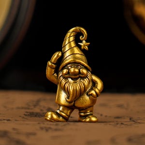 May include: A golden gnome figurine with a pointed hat and a star on top. The gnome has a long beard and is smiling, with one hand raised in a greeting gesture. The figurine is made of a shiny, metallic material.