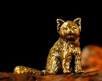 Könnte beinhalten: Eine detaillierte, goldfarbene Katzenfigur. Die Katze sitzt aufrecht mit zur Seite gerollter Schwanz. Die Figur hat strukturiertes Fell und ist vor einem dunklen Hintergrund platziert. Die Katze ist aus Metall und ein dekoratives Objekt.
