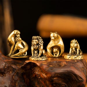 May include: Four small brass animal figurines arranged in a row. The set includes a seated dog, a lion with a cub, a bear with a cub, and a wolf with a cub. Each metallic sculpture features a polished gold-toned finish and detailed, smooth surfaces.