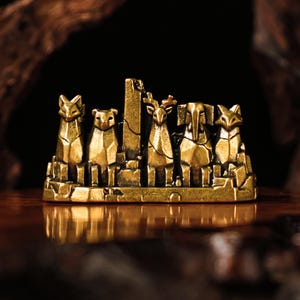 以下が含まれることがあります： キツネ、クマ、シカ、ゾウなどの様式化された動物の姿が特徴の、詳細な金色の彫刻。これらの姿は、質感のある、古びた外観の長方形の台座に配置されています。この彫刻はヴィンテージ感があります。